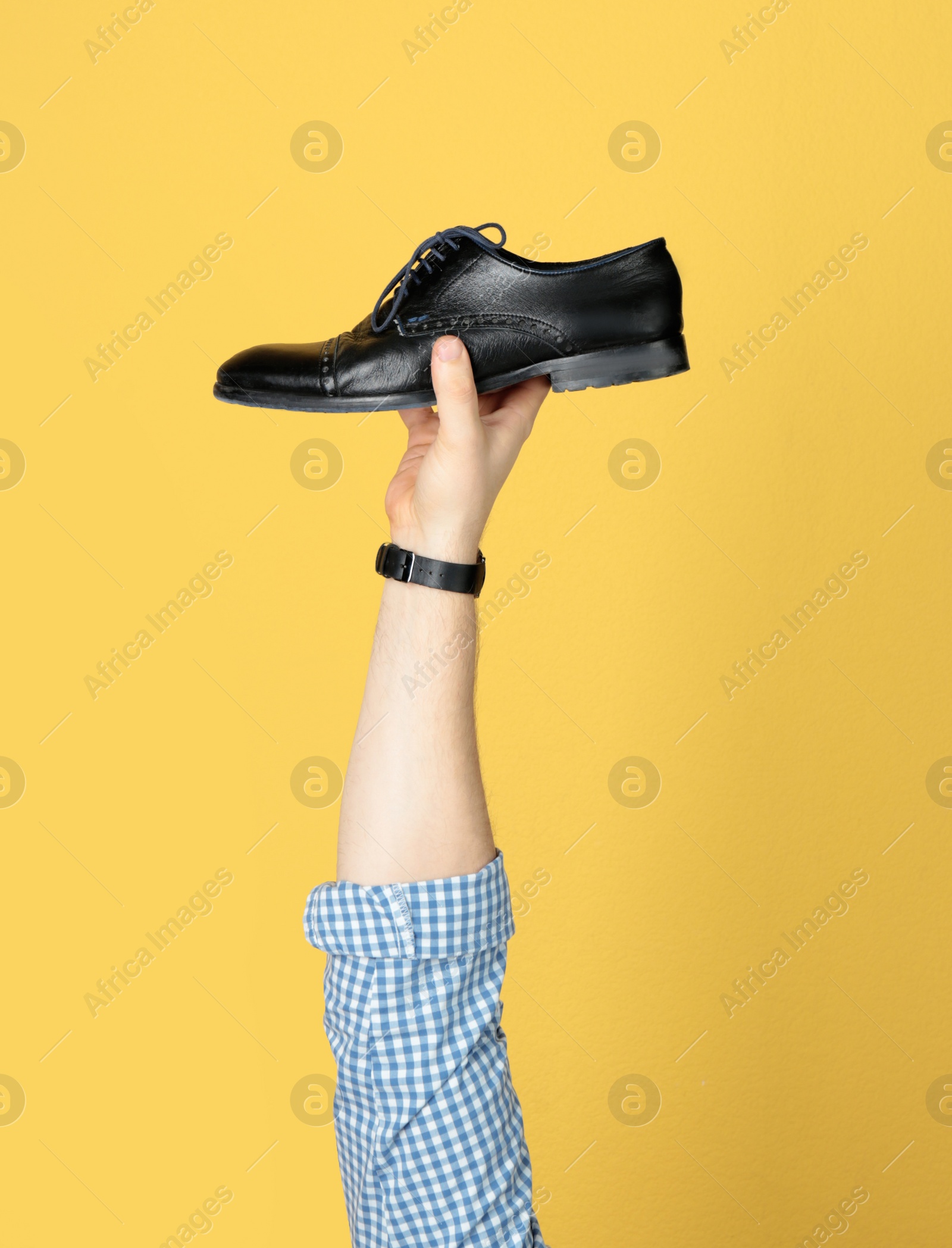 Photo of Man holding stylish shoe on yellow background, closeup