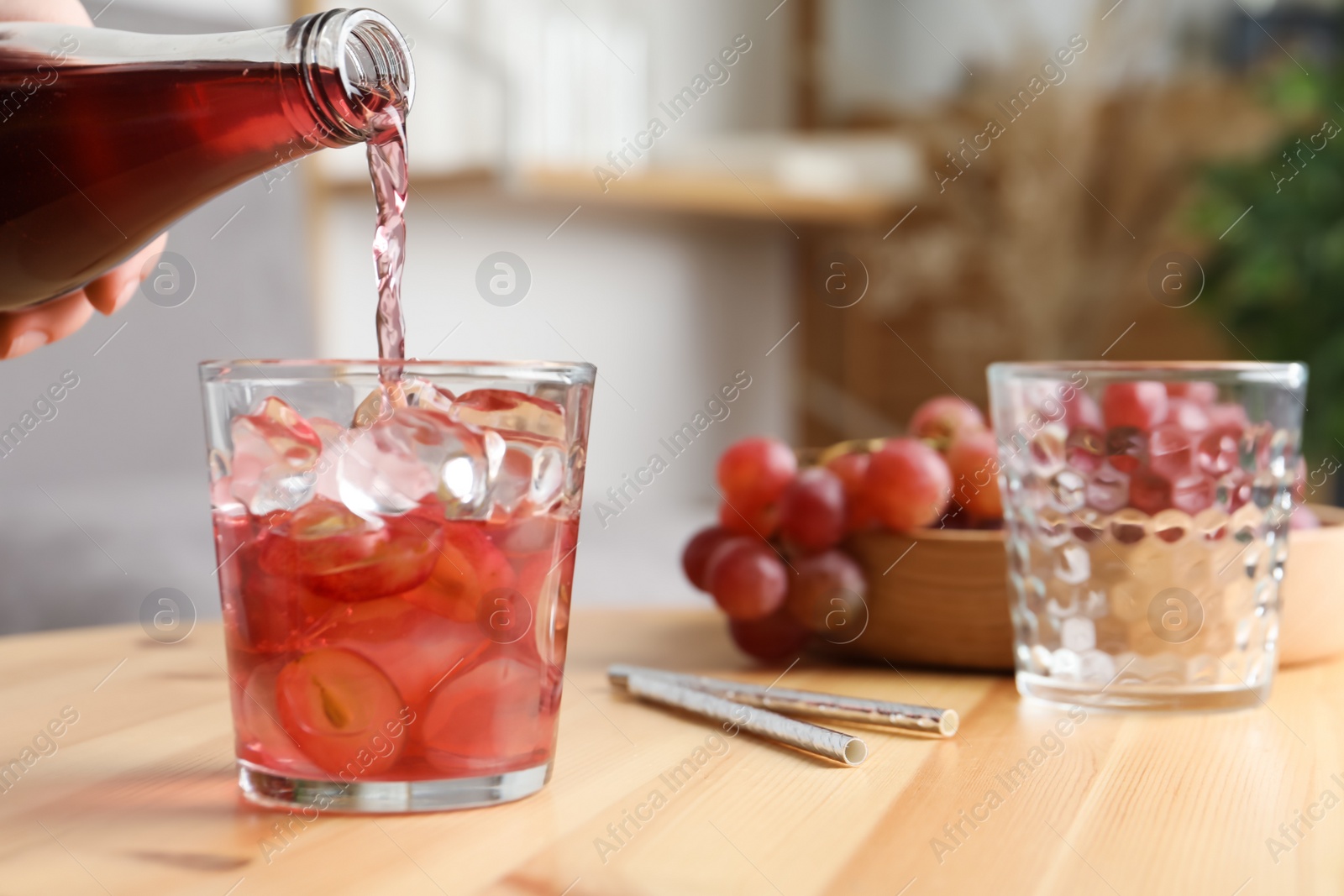 Photo of Woman pouring grape soda water into glass at wooden table indoors, closeup. Refreshing drink