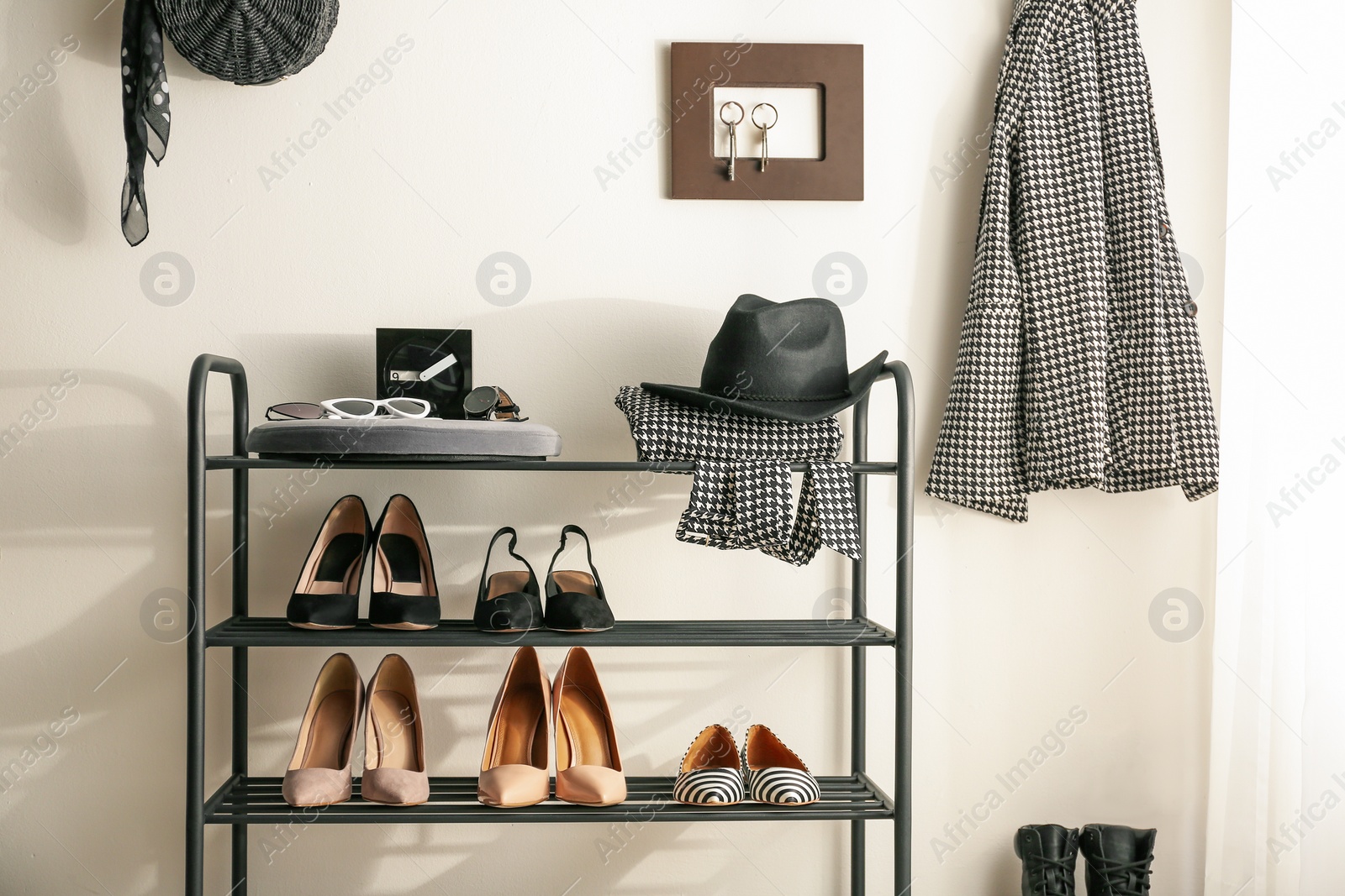 Photo of Black shelving unit with shoes and different accessories near white wall in hall