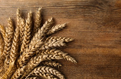 Photo of Ears of wheat on wooden table, flat lay. Space for text