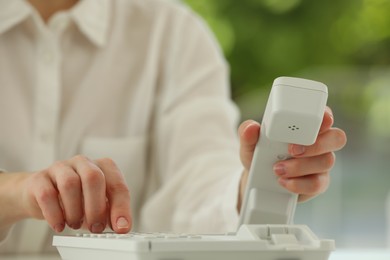 Photo of Assistant dialing number on telephone against blurred background, closeup