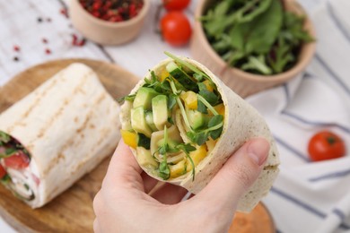 Photo of Woman holding delicious sandwich wraps with fresh vegetables at white wooden table, closeup
