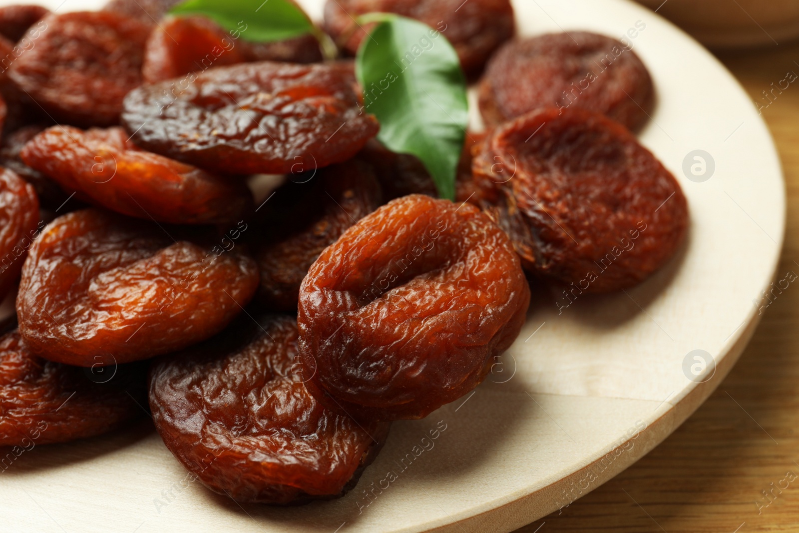 Photo of Plate of tasty apricots and green leaves on wooden table, closeup. Dried fruits