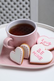 Photo of Delicious heart shaped cookies and cup of tea on white table