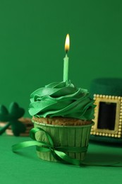 Photo of St. Patrick's day party. Tasty cupcake with burning candle and leprechaun hat on green background, closeup