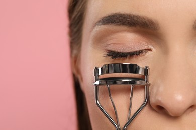 Photo of Woman with eyelash curler on pink background, closeup. Space for text
