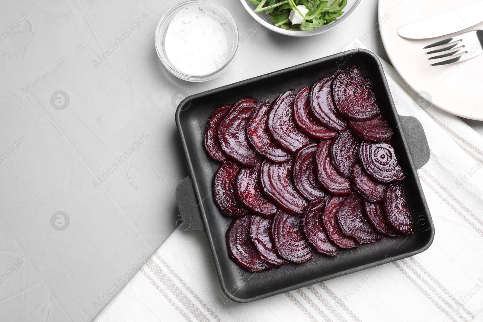 Photo of Baking dish with roasted beetroot slices on light grey table, flat lay