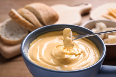 Photo of Dipping bread into pot with cheese fondue on table, closeup