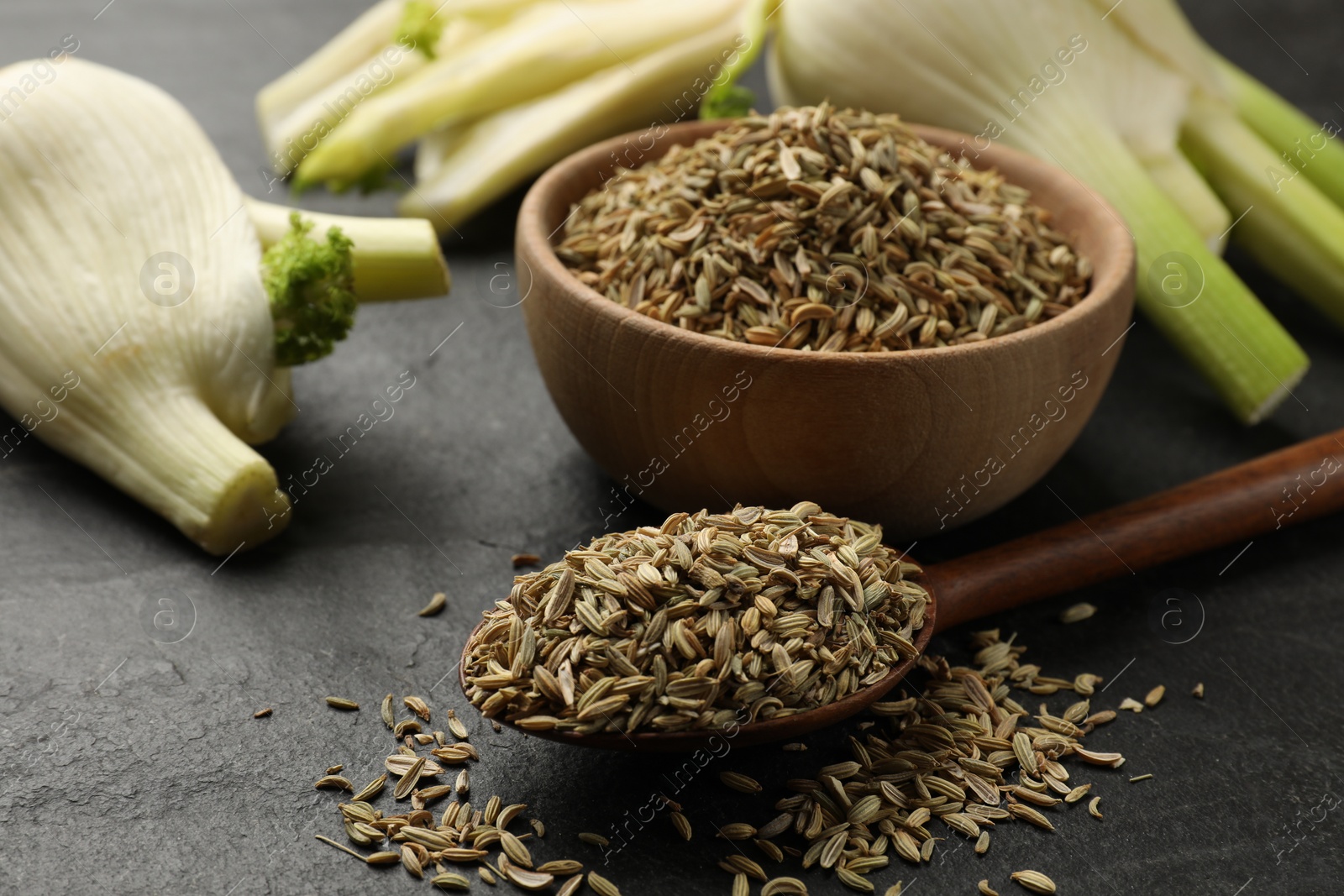 Photo of Fresh fennel bulbs, bowl and spoon with seeds on gray table, closeup