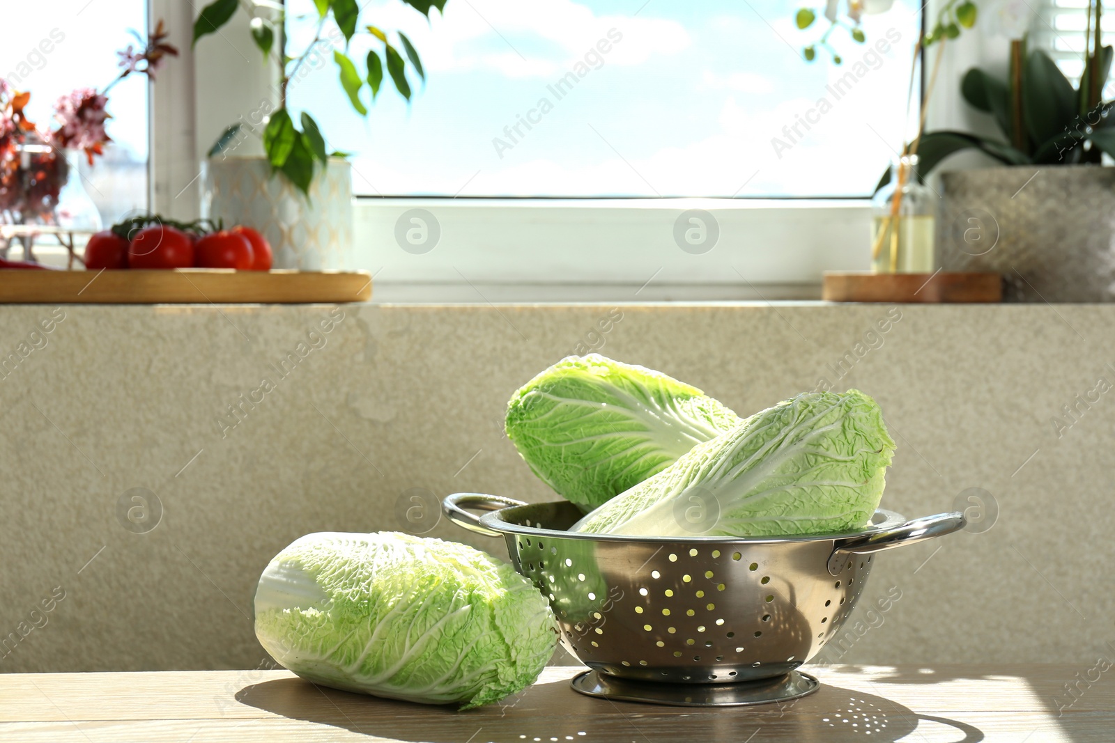 Photo of Fresh Chinese cabbages and colander on light wooden table indoors