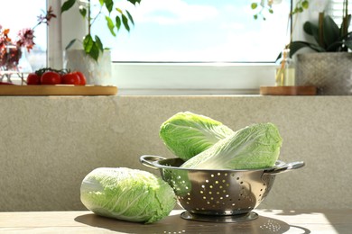 Photo of Fresh Chinese cabbages and colander on light wooden table indoors