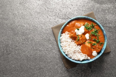 Photo of Delicious butter chicken with rice in bowl on grey background, top view. Space for text