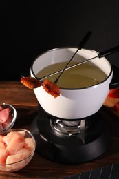 Photo of Fondue pot, forks with fried meat pieces and other products on wooden table