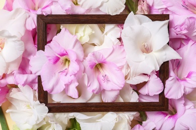 Photo of Top view of wooden frame and beautiful gladiolus flowers as background, closeup