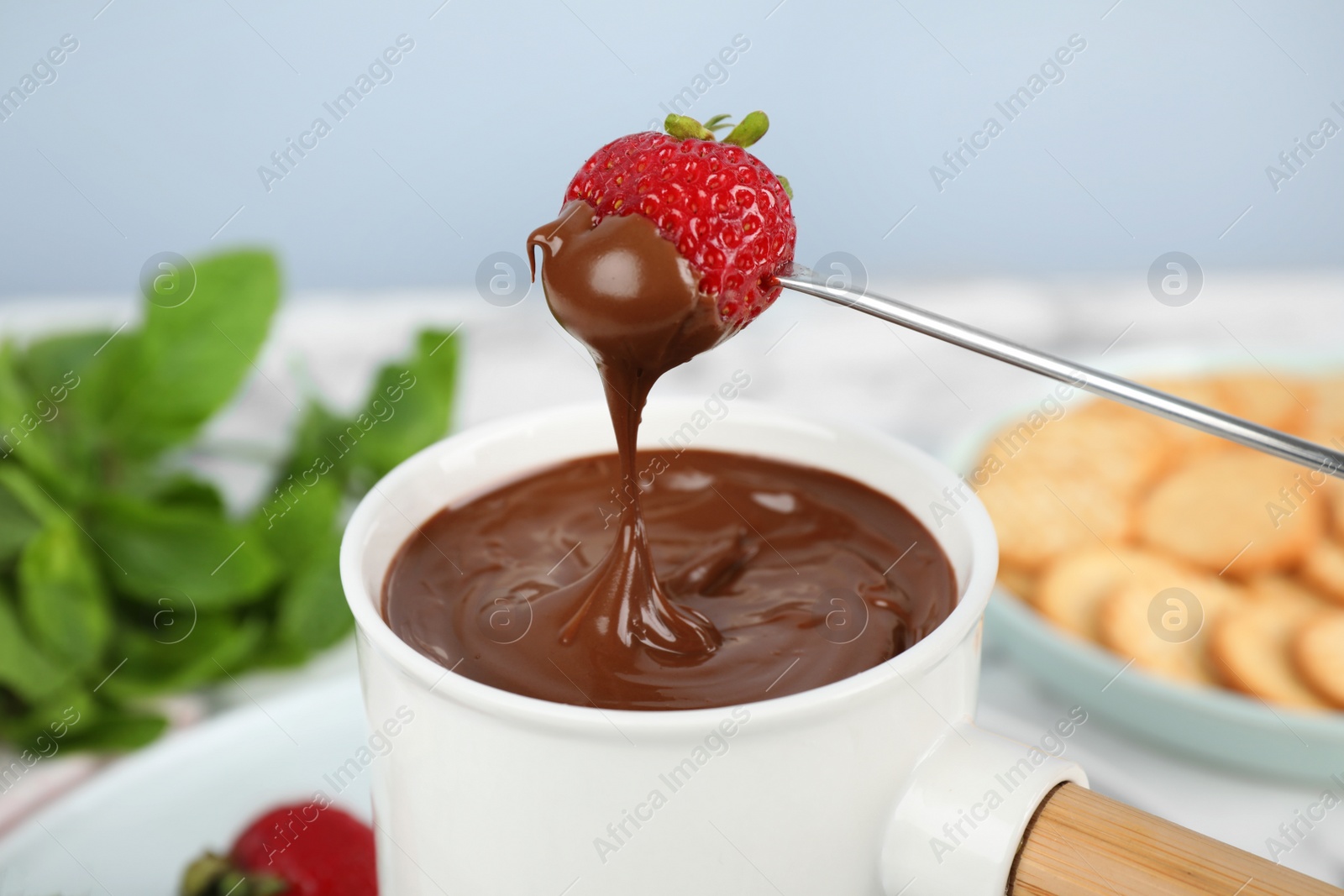 Photo of Fondue pot with chocolate and strawberry on table, closeup