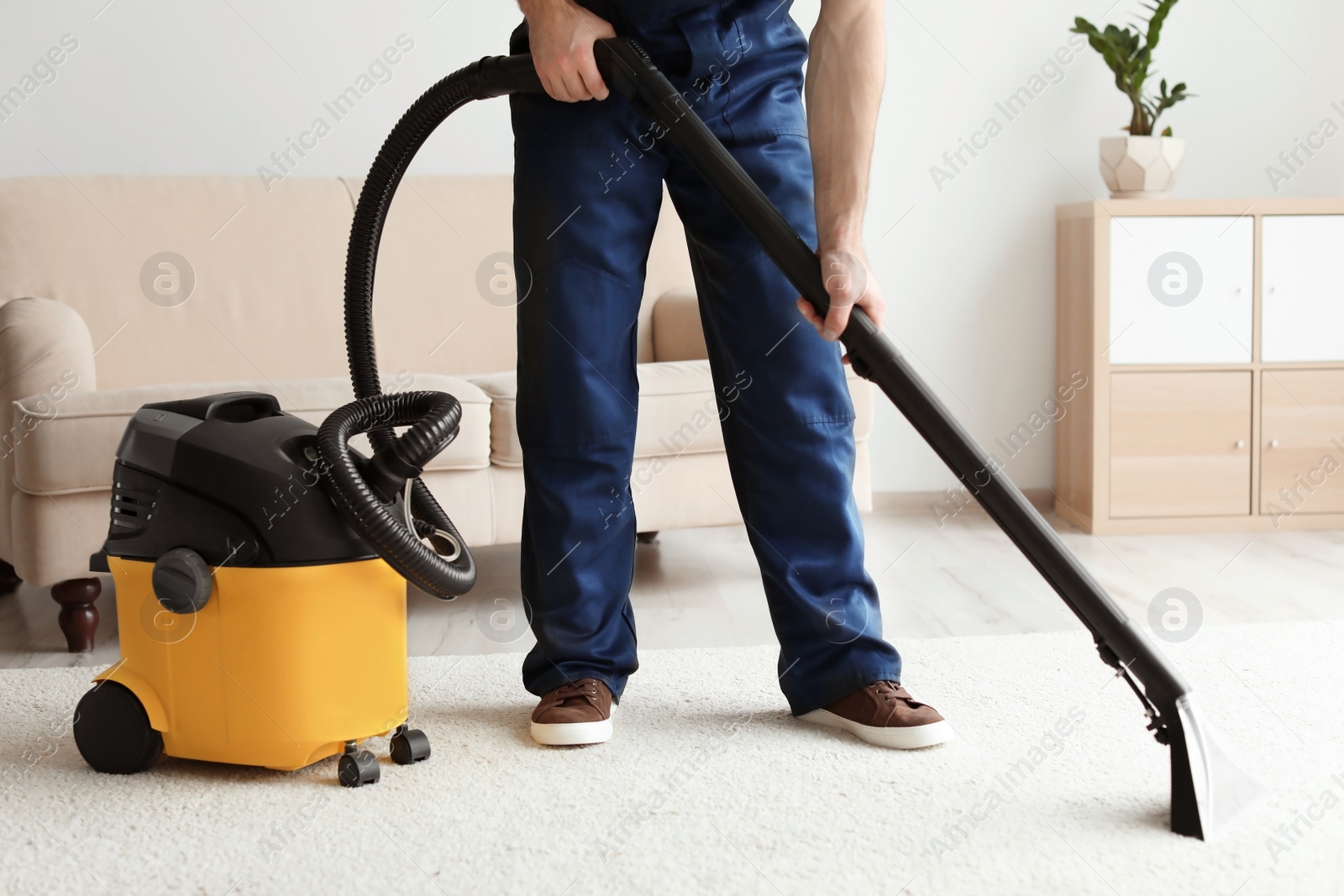 Photo of Male worker cleaning carpet with vacuum in living room