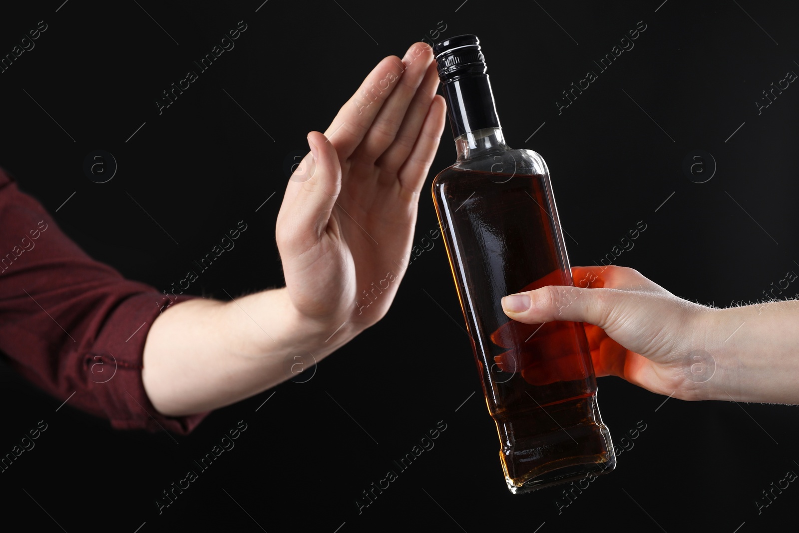 Photo of Alcohol addiction. Woman refusing bottle of whiskey on black background, closeup