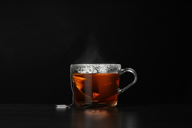 Photo of Glass cup of hot tea on table against black background, space for text