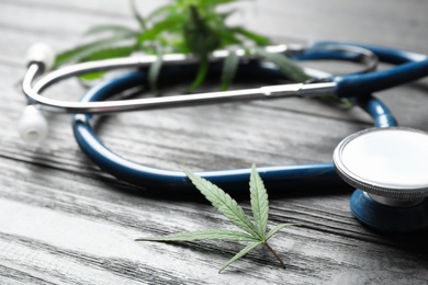 Photo of Hemp leaves and stethoscope on grey wooden table, closeup