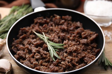 Photo of Fried ground meat in frying pan and rosemary on table, closeup