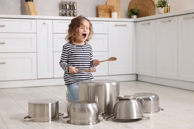 Photo of Little girl pretending to play drums on pots in kitchen