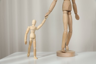 Wooden mannequins of parent with child on white table against light background. Family Day