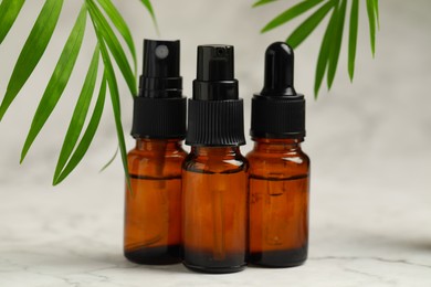 Bottles of organic cosmetic products and green leaves on light background