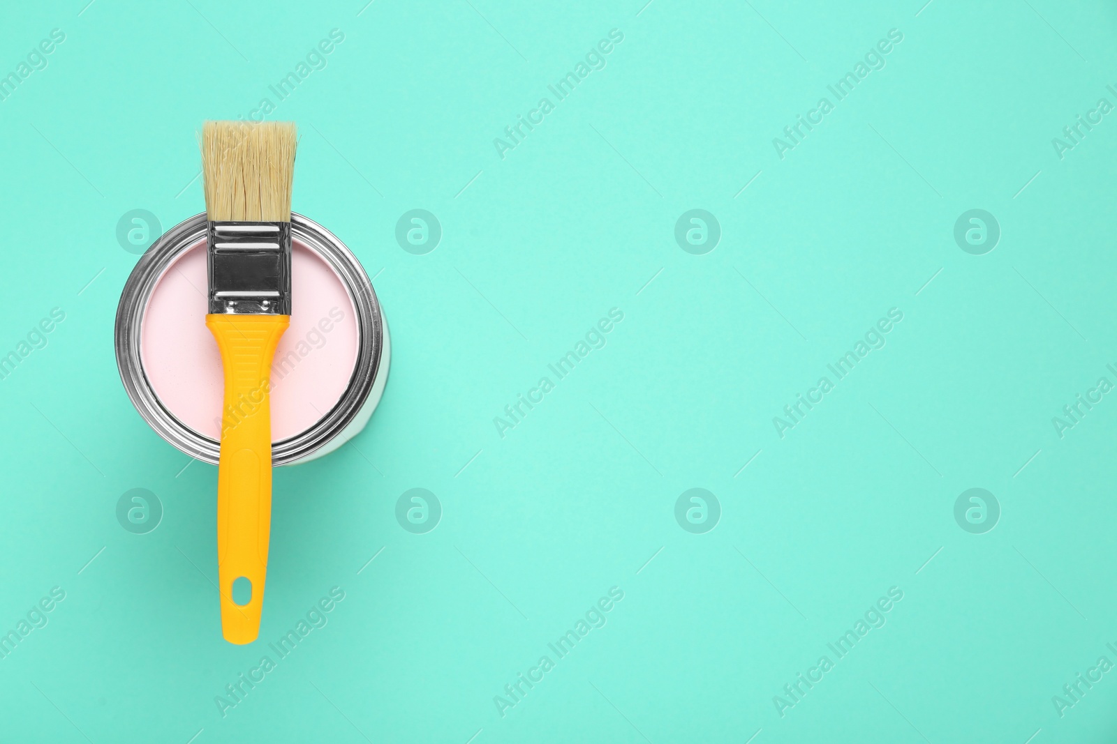 Photo of Can of pink paint with brush on turquoise background, top view. Space for text