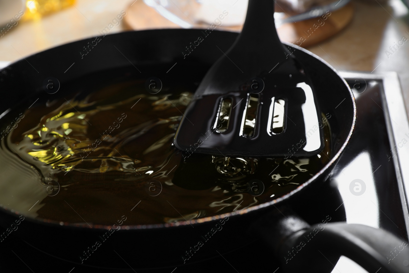 Photo of Frying pan with used cooking oil and spatula on stove, closeup