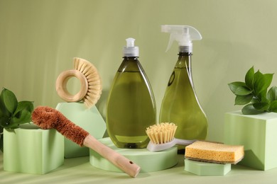 Bottles of cleaning product, sponge and brushes on light green background