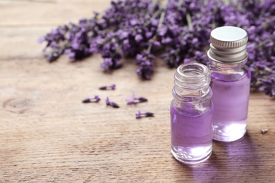 Photo of Glass bottles of natural cosmetic oil and lavender flowers on wooden table, space for text