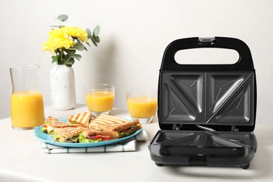 Photo of Modern grill maker and sandwiches on white table