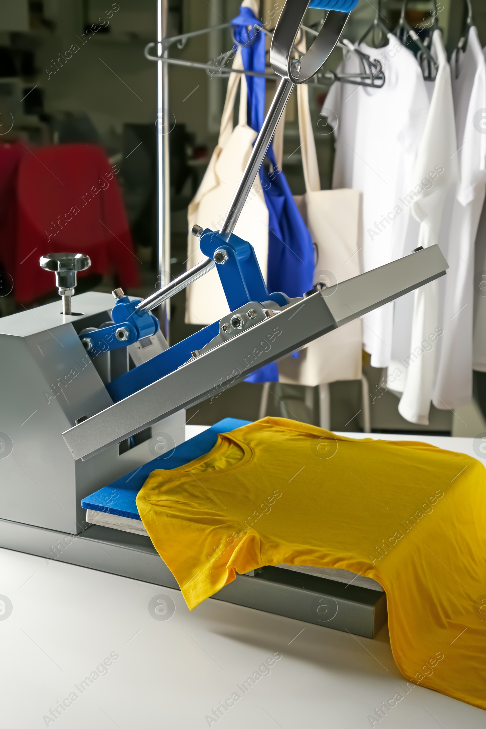 Photo of Printing logo. Heat press with yellow t-shirt on white table