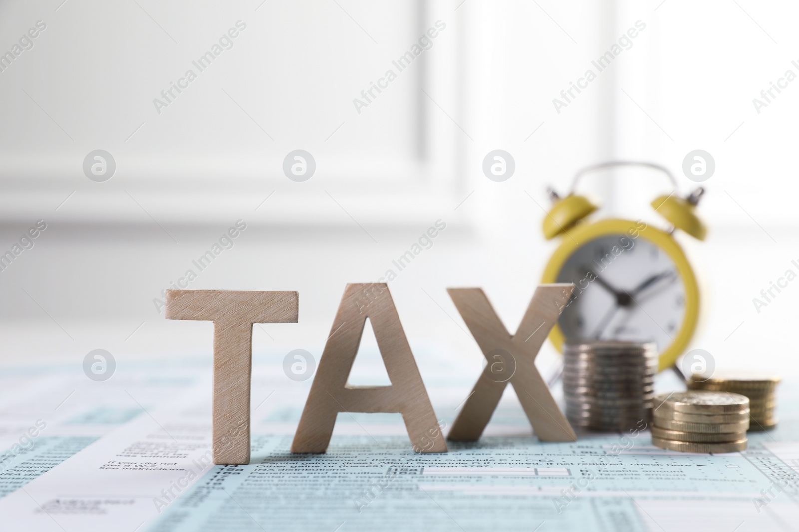 Photo of Word Tax made with wooden letters, coins and alarm clock on document against light background