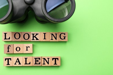 Photo of Staff recruitment concept. Phrase Looking For talent made of wooden cubes and binoculars on green background, flat lay. Space for text
