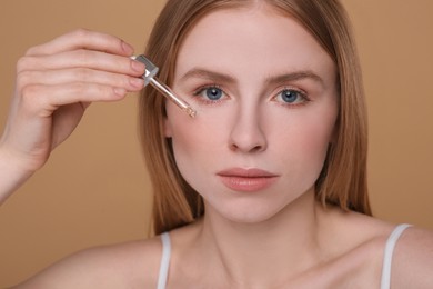 Photo of Woman applying essential oil onto face on light brown background