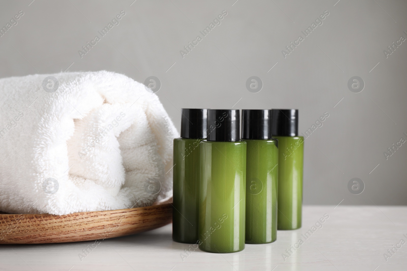 Photo of Mini bottles with cosmetic products and towel on white table against grey background