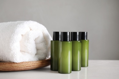 Mini bottles with cosmetic products and towel on white table against grey background