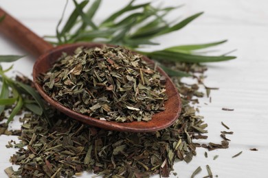 Spoon of dry tarragon and fresh leaves on white wooden table, closeup