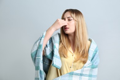 Young woman with blanket suffering from runny nose on light background
