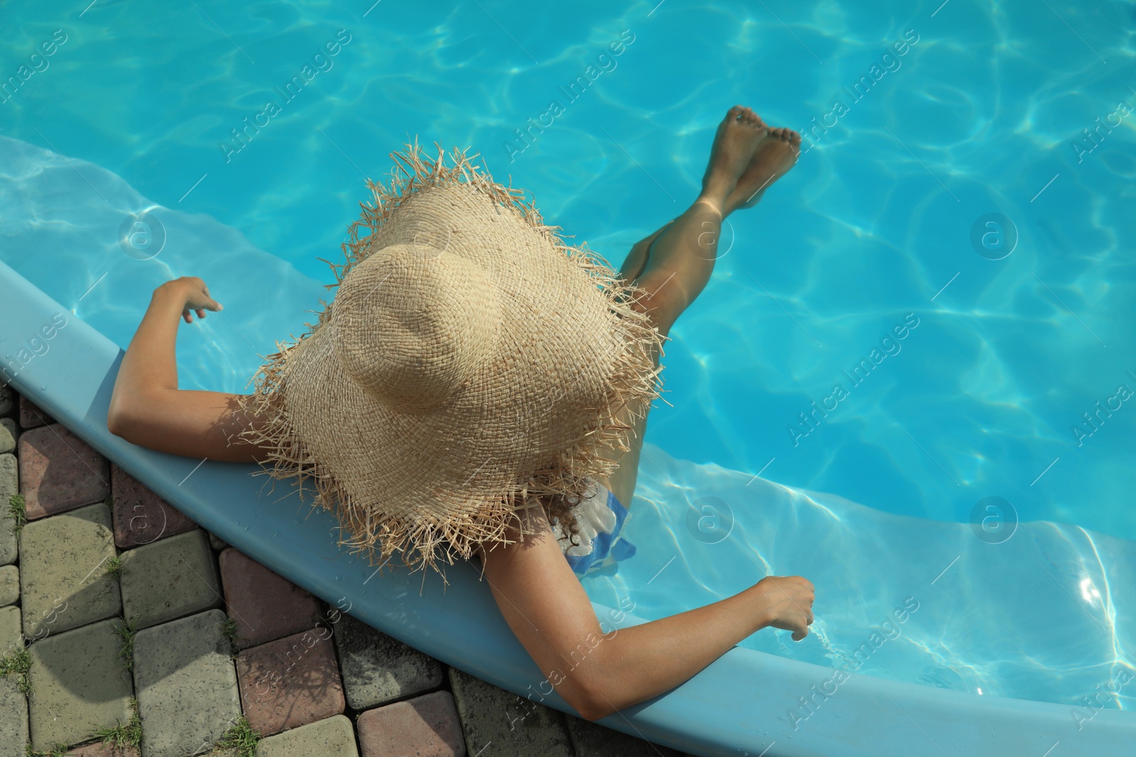 Photo of African American woman with straw hat resting in outdoor swimming pool on sunny summer day, top view