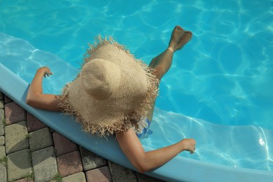 African American woman with straw hat resting in outdoor swimming pool on sunny summer day, top view