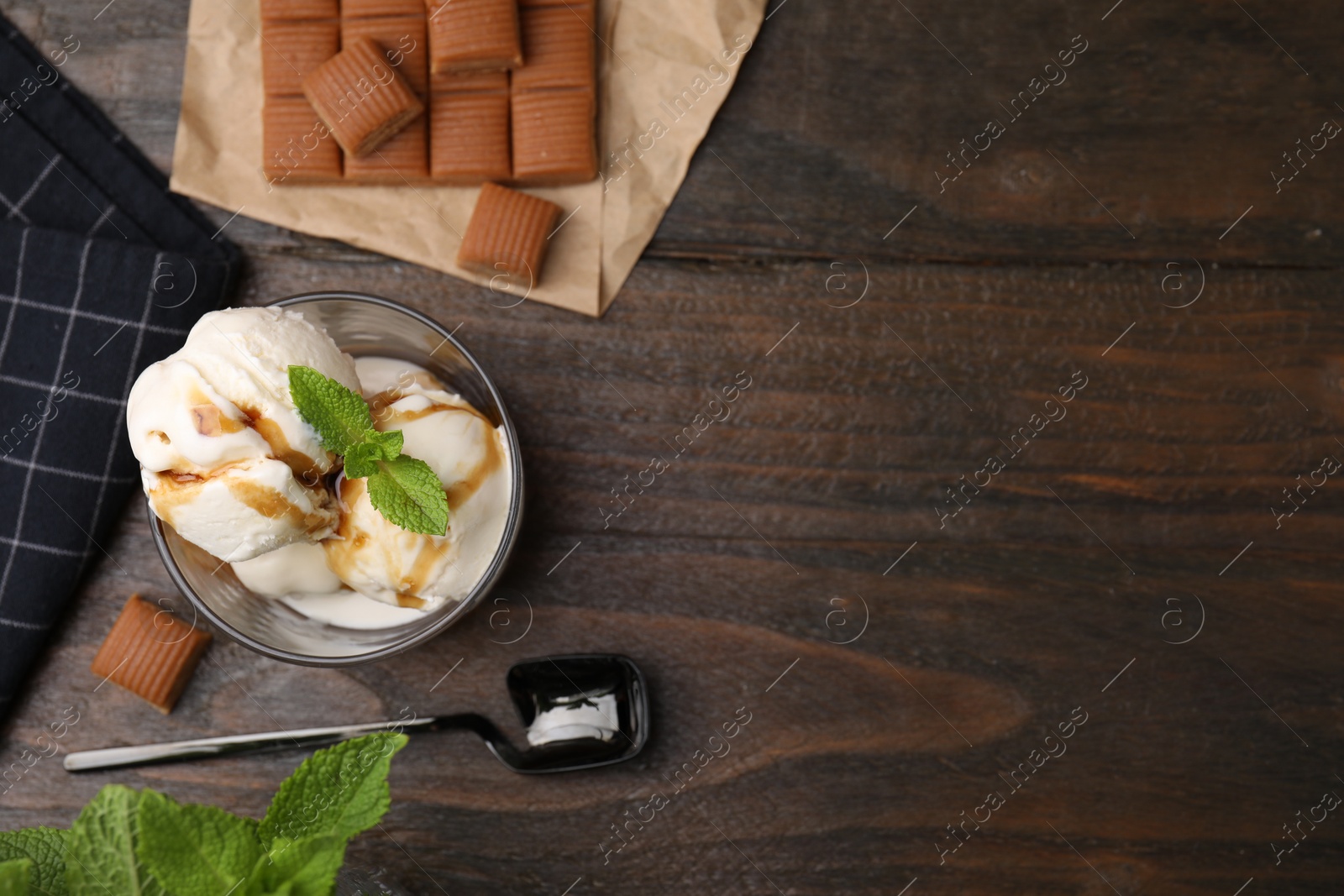 Photo of Scoops of ice cream with caramel sauce, mint leaves and candies on wooden table, flat lay. Space for text