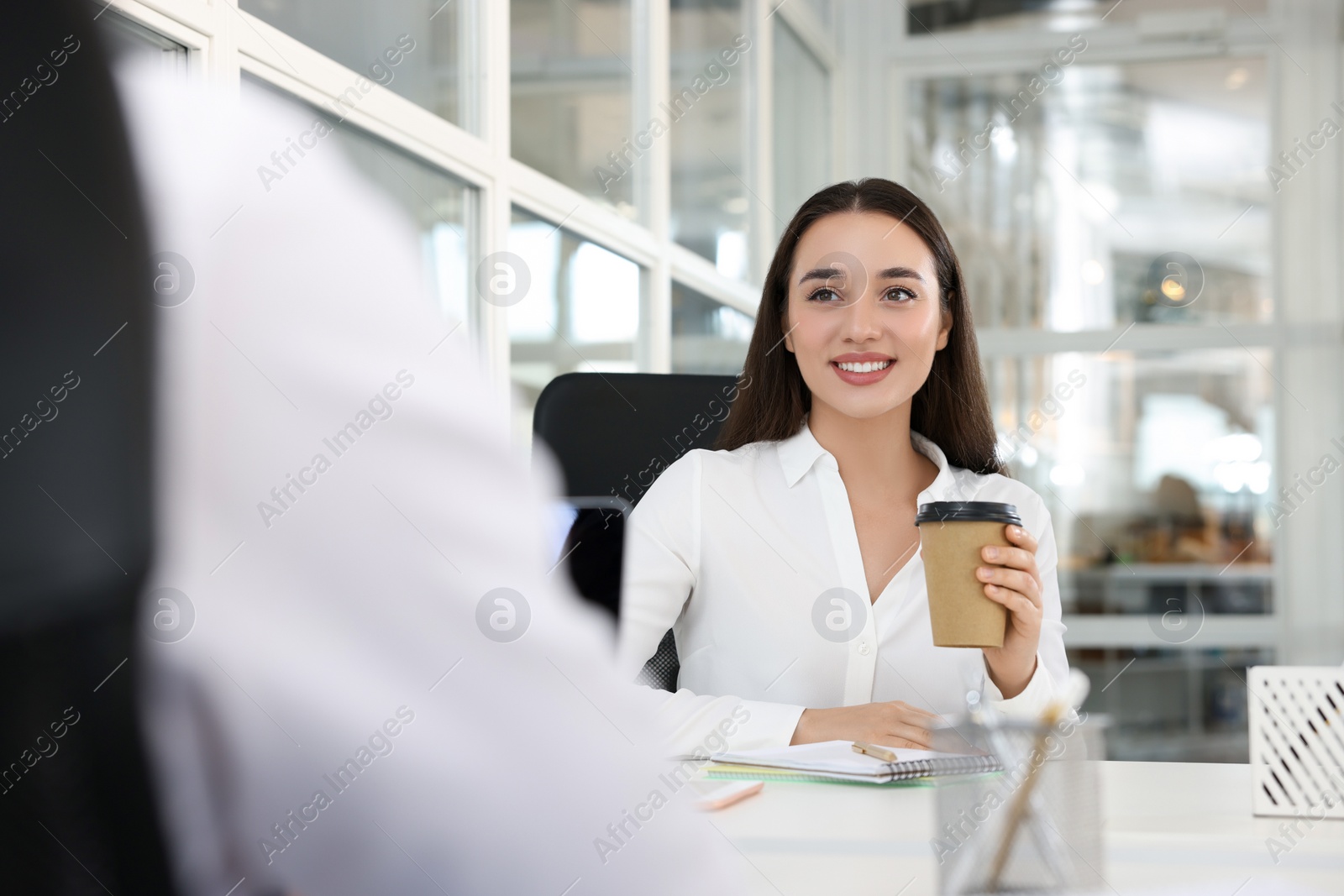 Photo of Happy woman with paper cup of coffee at desk in open plan office