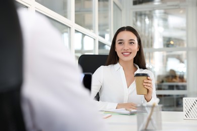 Happy woman with paper cup of coffee at desk in open plan office