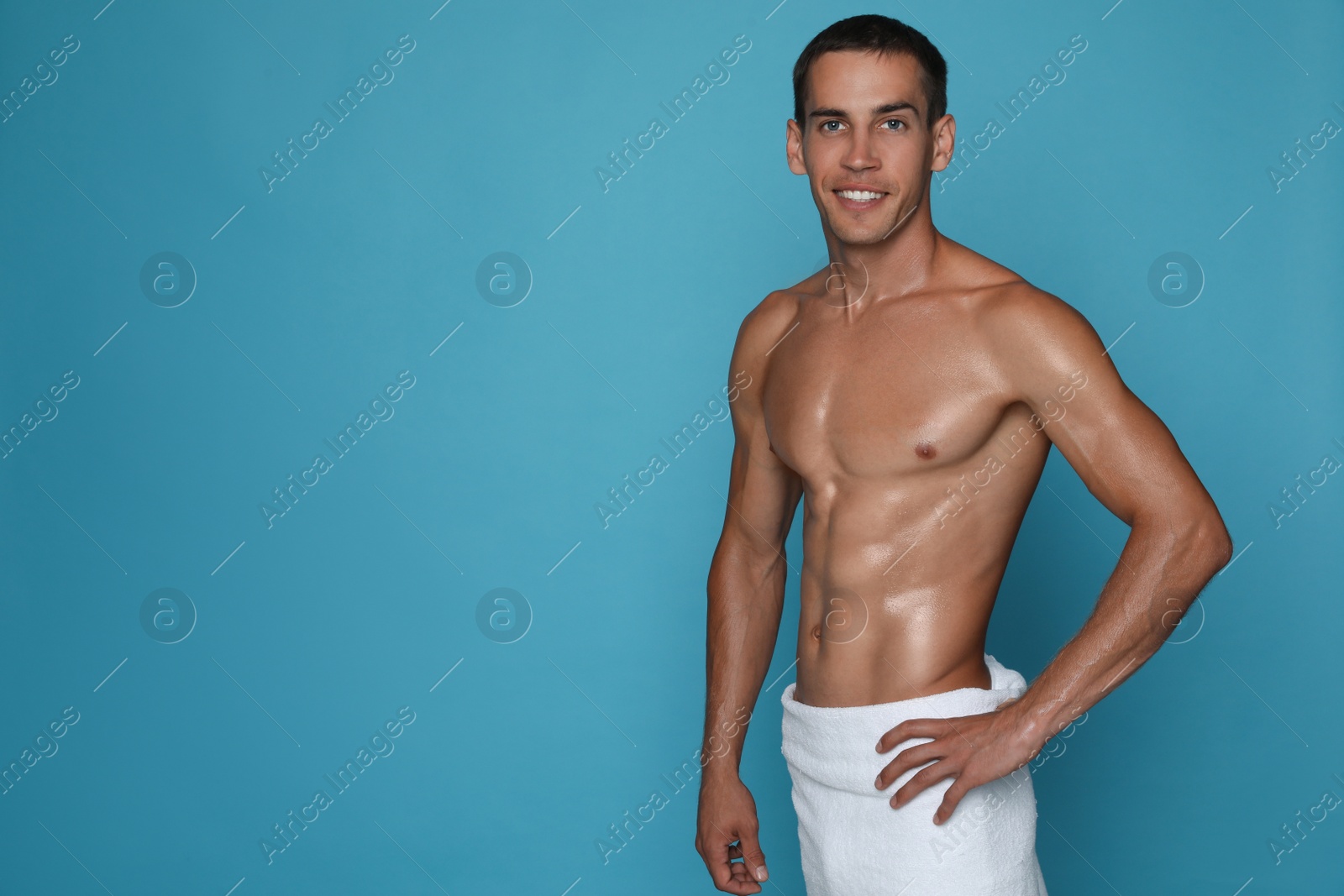 Photo of Handsome shirtless man with slim body and towel wrapped around his hips on light blue background. Space for text