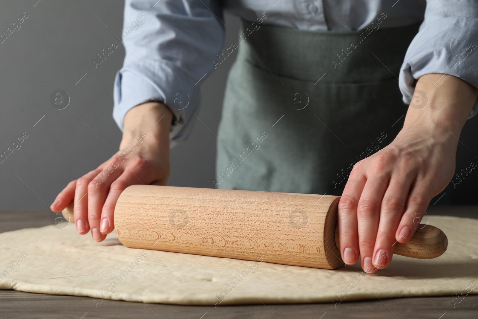 Photo of Woman rolling raw dough at wooden table, closeup