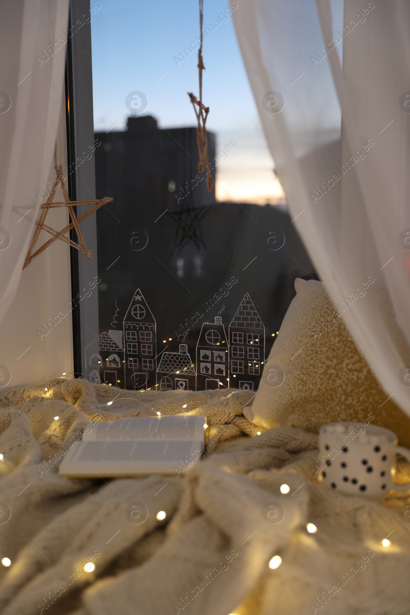 Photo of Open book and cup of hot drink on plaid near window with beautiful drawing at home. Christmas decor