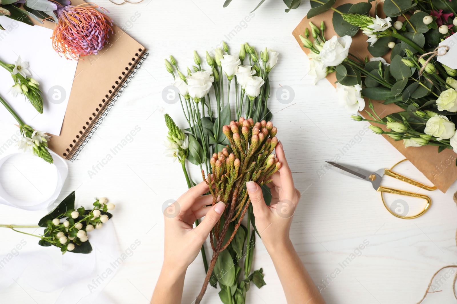 Photo of Florist making beautiful bouquet at white wooden table, top view