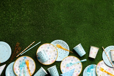 Photo of Disposable tableware on green artificial grass, flat lay. Space for text